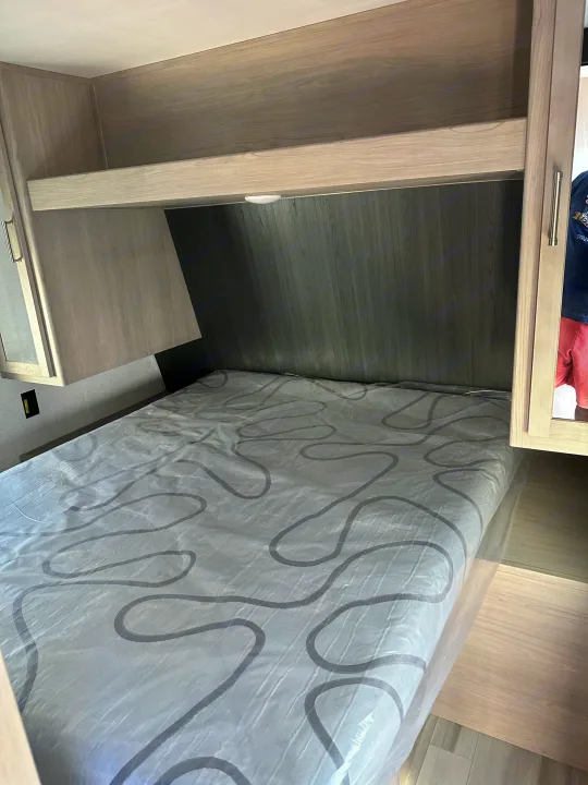 Clean RV rental bedroom featuring a new bed, overhead storage, and modern wood finishes. Ready for your next adventure.. Keystone RV SG261BHC 2024