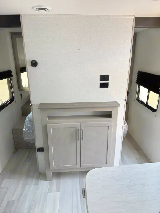 Inside an RV rental, a divider wall with TV hookups and built-in light wood cabinetry separates living and bedroom areas.. Keystone RV SG261BHC 2024