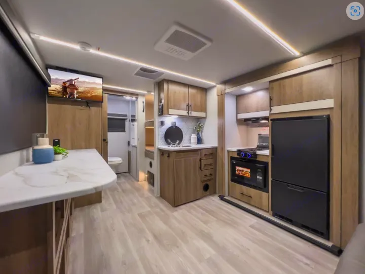 Modern RV rental interior featuring a well-equipped kitchen, spacious living area with TV, and light wood cabinetry.. Grand Design Imagine AIM 2024