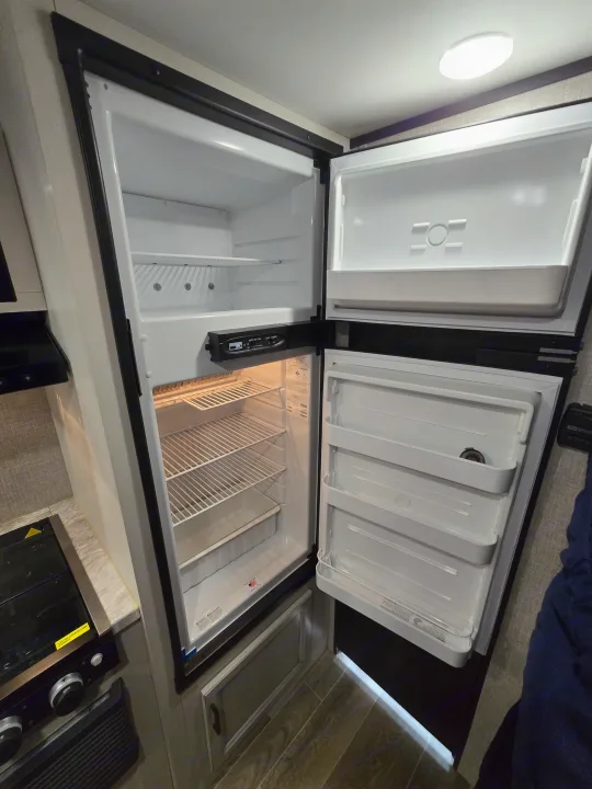 Inside an RV rental kitchen: a clean, open refrigerator/freezer and stovetop.. Jayco Jay Flight SLX 2022
