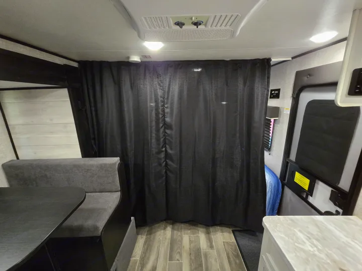 RV rental interior with a gray dinette, a large black partition curtain, and overhead AC for a comfortable living space.. Jayco Jay Flight SLX 2022