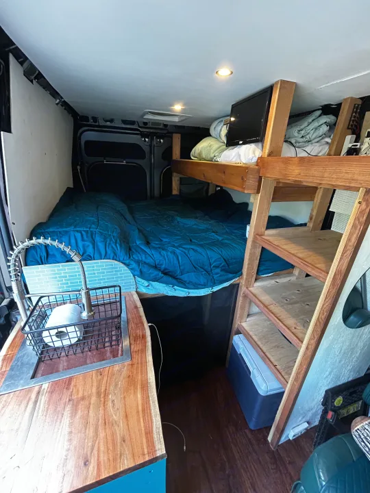 Explore this RV rental's clever interior: a cozy bed, kitchen sink, and overhead bunk for compact living on the go.. Dodge Ram 1500 2017