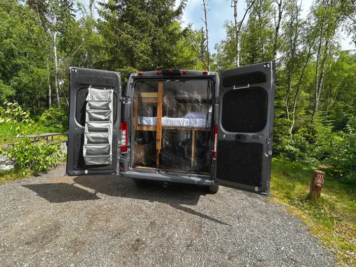 Explore this RV rental camper van with open rear doors revealing bunk beds, parked at a scenic campsite.. Dodge Ram 1500 2017