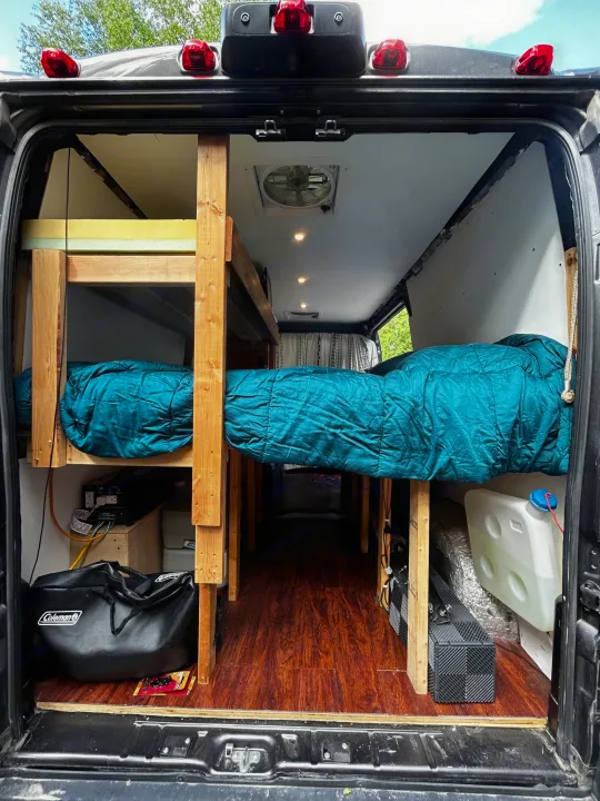 Interior view of an RV rental camper van from the back, revealing custom wooden bunk beds, a single bed, and amenities.. Dodge Ram 1500 2017
