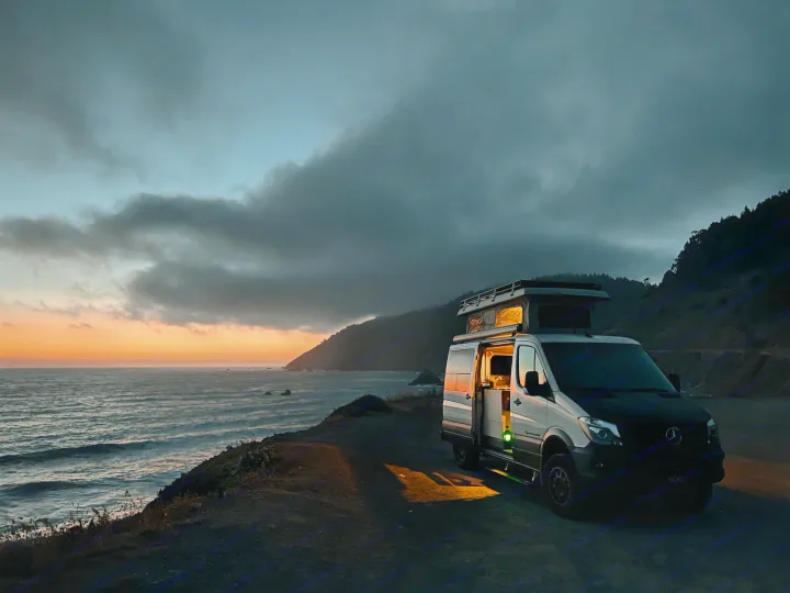 An RV rental camper van at a dramatic coastal sunset, warm light from inside illuminates the ocean overlook.. Sportsmobile Regular Body 4X4 2017