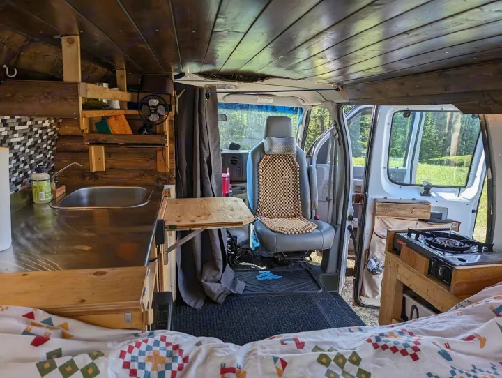 This converted van interior for rv rental features a compact kitchen, bed, and stove, perfect for travel adventures.. Ford Econoline E250supercab 2012