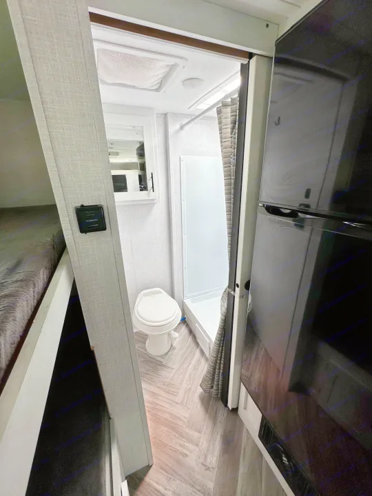 Explore this RV rental's clever interior: compact bathroom with shower/toilet, bunk beds, & large fridge.. Dutchmen Coleman Rubicon 2023