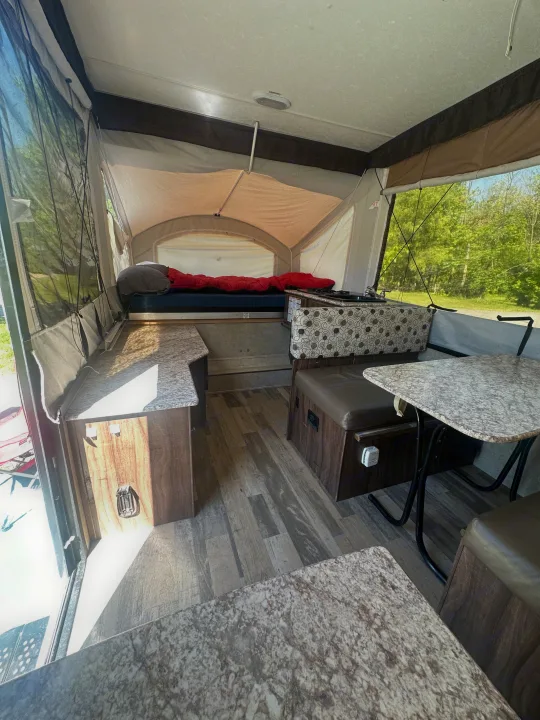 Inside a bright pop-up RV rental. View shows a dinette, bed, and kitchen counter with wood-look flooring.. coachmen clipper 2018