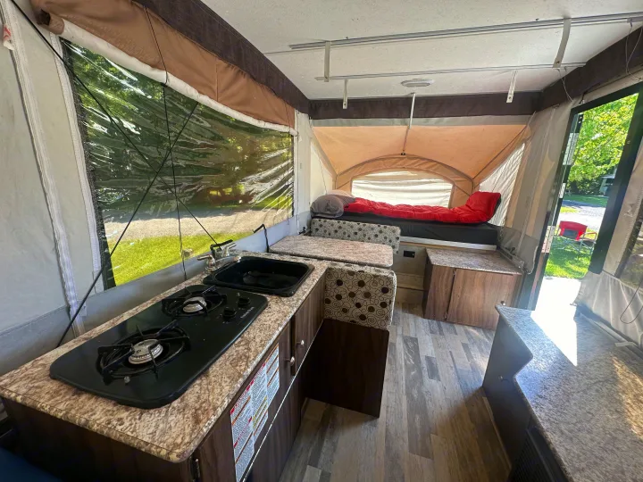 Step inside this pop-up RV rental: a compact interior featuring a kitchen with stove/sink, dining booth, and comfortable bed.. coachmen clipper 2018