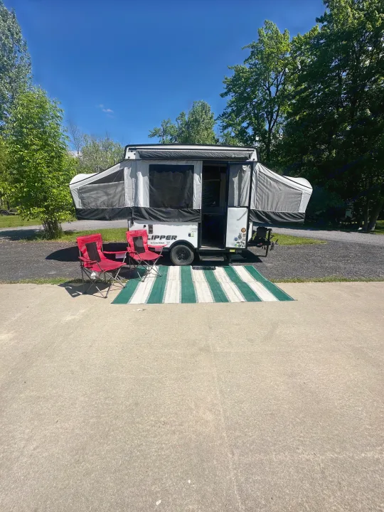 Set up for a sunny camping trip, this pop-up camper RV rental includes outdoor chairs and a mat, ready for adventure.. coachmen clipper 2018