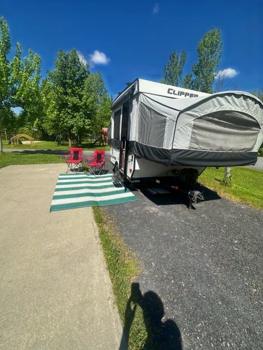 A pop-up camper rv rental set up at a sunny campsite with chairs & mat, ready for outdoor fun.. coachmen clipper 2018