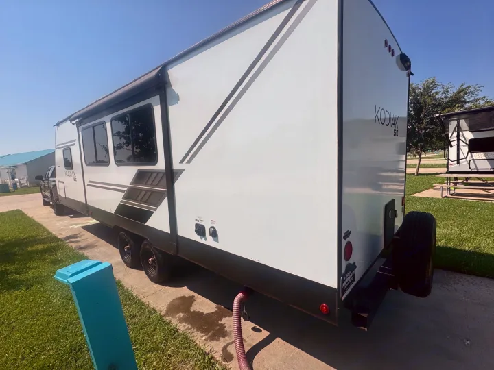 A white Kodiak SE travel trailer, likely an RV rental, parked and hooked up at a sunny campsite.. Dutchmen Kodiak SE 2024