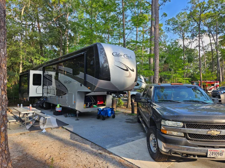 Relaxing at a shady RV campsite with a large fifth-wheel & truck. Perfect for your next rv rental adventure!. Cedar Creek Silverback 2020