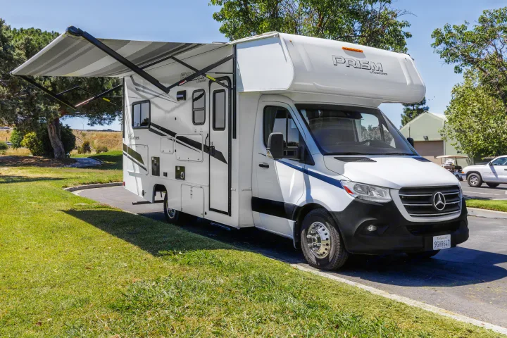 White Mercedes-Benz rv rental with extended awning, parked outdoors. Perfect for travel and camping adventures.. Coachmen Prism 2023