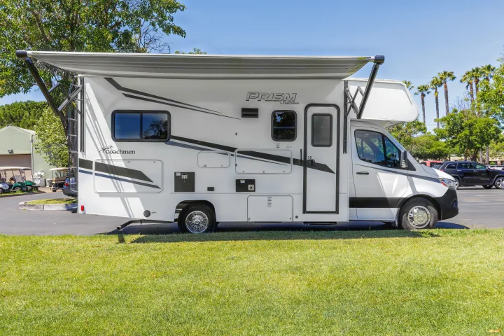 White Coachmen Prism RV rental with an extended awning, parked on grass. Ideal for travel and outdoor living.. Coachmen Prism 2023