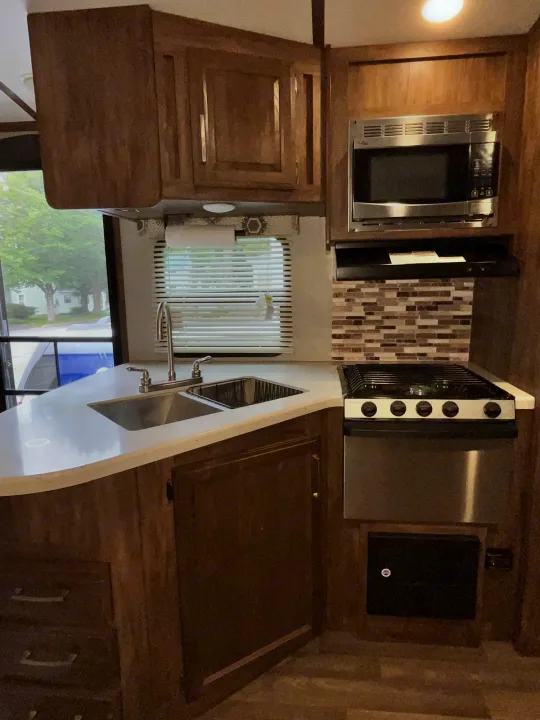 Well-equipped RV rental kitchen featuring a double sink, microwave, stove, and ample cabinet space.. Keystone RV Cougar X-Lite 2018