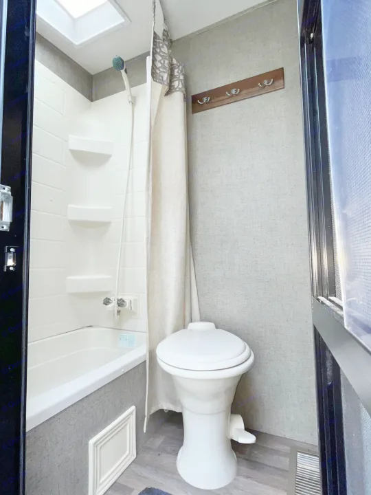 RV rental bathroom featuring a compact shower/tub, toilet, and coat rack, perfect for travel comfort.. Keystone RV Cougar X-Lite 2018