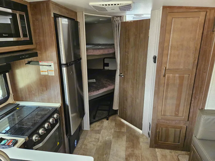 Spacious RV rental interior with full kitchen (microwave, stove, fridge), cozy bunk beds, and wood-paneled walls.. Forest River Flagstaff Micro Lite 2023