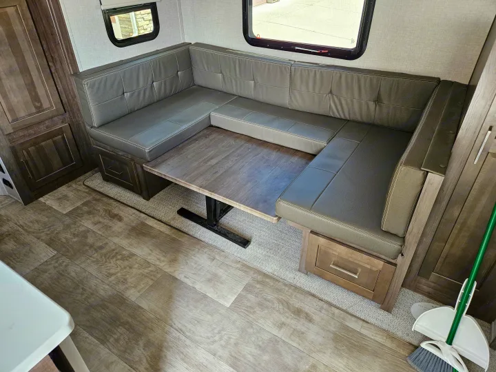 Inside an RV rental: a cozy dinette area with gray U-shaped seating, a wooden table, under-seat storage, and wood-look flooring.. Forest River Flagstaff Micro Lite 2023