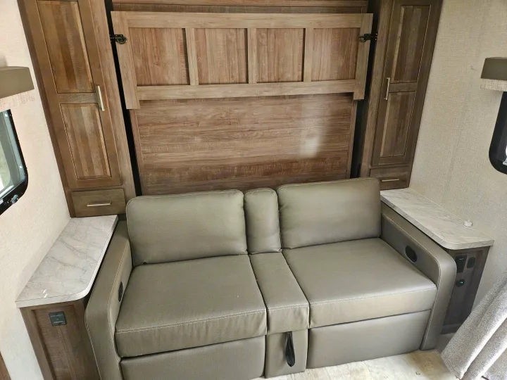 An RV rental showcases a convertible sofa and a folded murphy bed, offering versatile sleeping and living space.. Forest River Flagstaff Micro Lite 2023