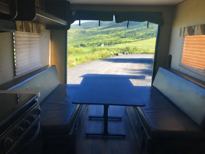 View from an RV rental dinette: table, benches, and wide-open scenic landscape with green hills and a gravel road.. Forest River Cherokee Grey Wolf Toy Hauler 2016