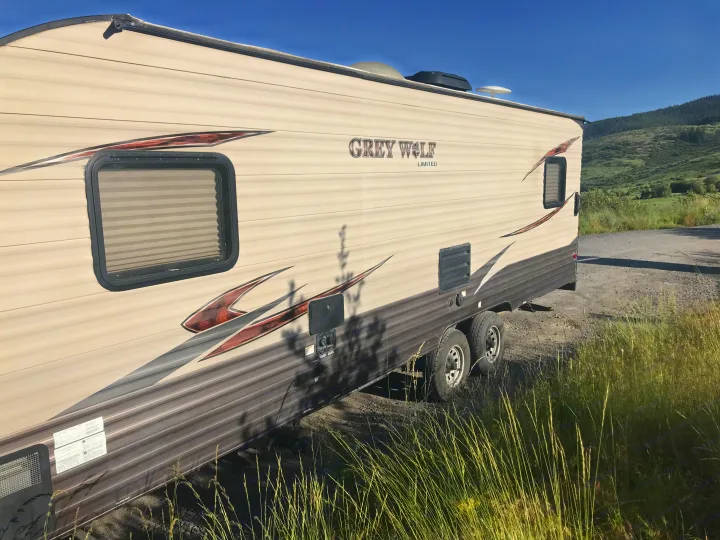 This "Grey Wolf Limited" travel trailer for rv rental is parked on a dirt path with green hills and blue sky.. Forest River Cherokee Grey Wolf Toy Hauler 2016