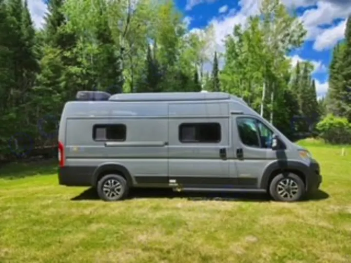 This grey camper van, ideal for an RV rental, is parked outdoors on a grassy area amidst trees, ready for adventure.. Winnebago Solis 2023