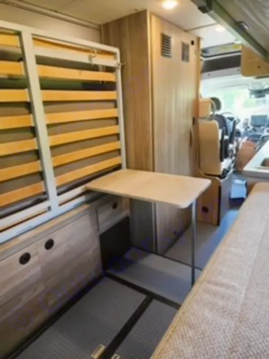 Compact **rv rental** interior: a foldable slatted bed, pull-out table, and integrated cabinets create an efficient living space.. Winnebago Solis 2023