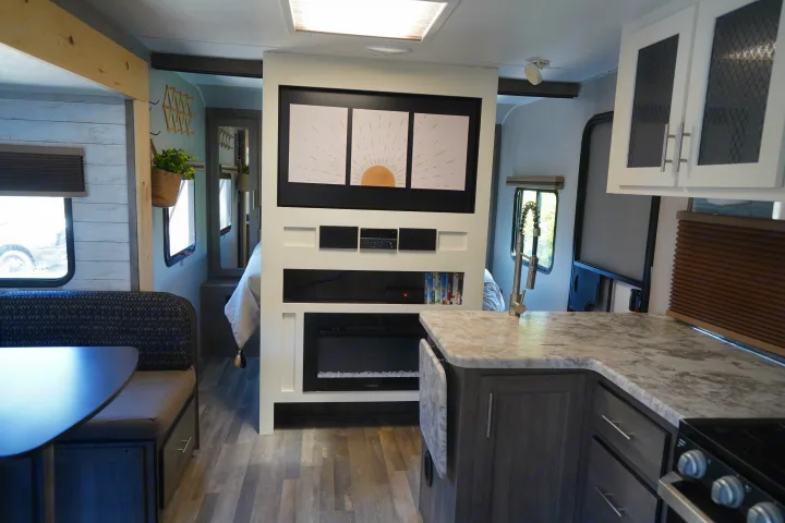 Modern RV rental interior: view of compact kitchen, dinette, and entertainment center with fireplace, looking towards the bedroom.. Forest River Vibe 2020