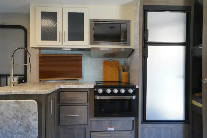 This RV rental kitchen offers a full range, microwave, refrigerator, and modern faucet for your adventures.. Forest River Vibe 2020