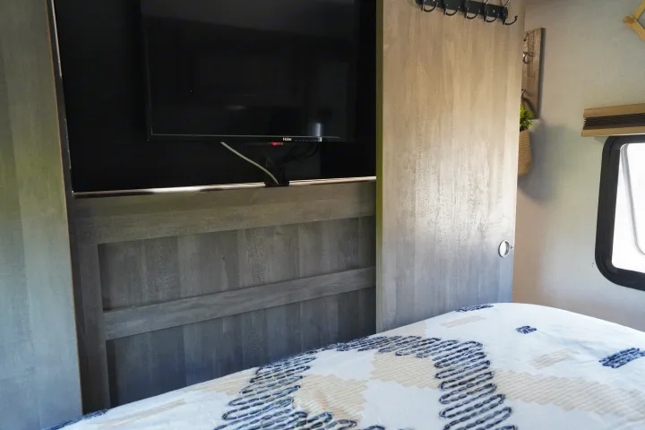 Inside an RV rental bedroom: A mounted TV, wood-paneled headboard, and sliding door. A patterned bed fills the foreground.. Forest River Vibe 2020