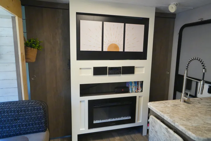 RV rental interior showcasing a compact entertainment center with art, fireplace, and a kitchen area.. Forest River Vibe 2020