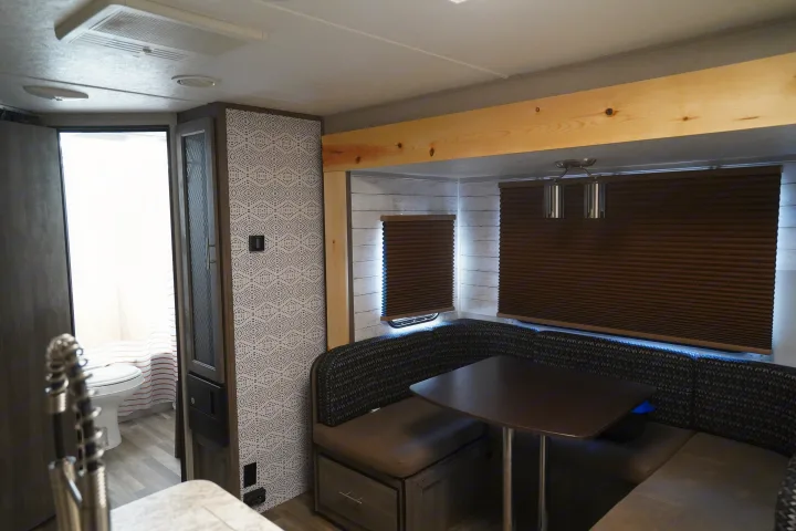 Modern RV rental interior: a comfy dinette, dark blinds, stylish wallpaper, and a bathroom view. Perfect for adventures.. Forest River Vibe 2020