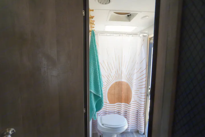 RV rental bathroom interior with a sunburst shower curtain, compact toilet, and a teal towel.. Forest River Vibe 2020