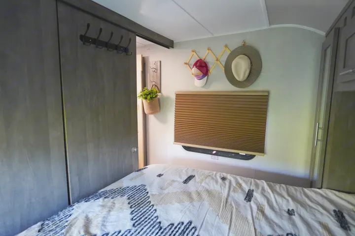 RV rental bedroom: patterned bed, window with blind & exit sign, and wall storage with hooks.. Forest River Vibe 2020