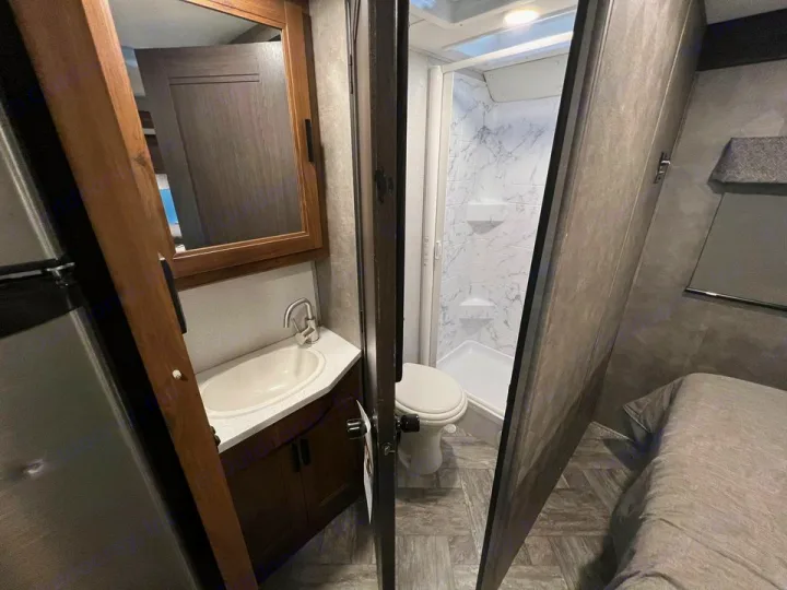 This RV rental features a compact interior: partial view of fridge, full bathroom (sink, toilet, shower), and bed.. Forester LE 2022