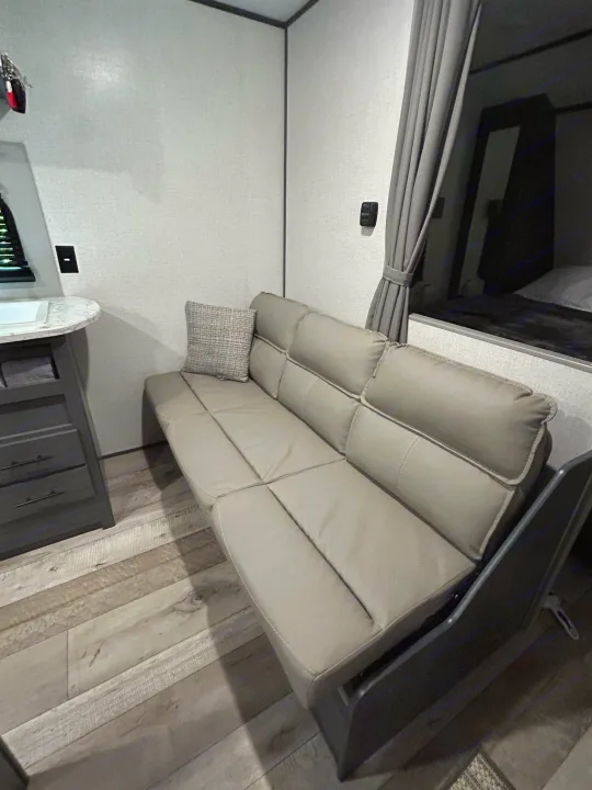 Explore comfort in this RV rental! Interior features a flexible sofa bed, compact kitchen prep area, and shaded sleeping nook.. Dutchmen Aspen Trail LE 2022