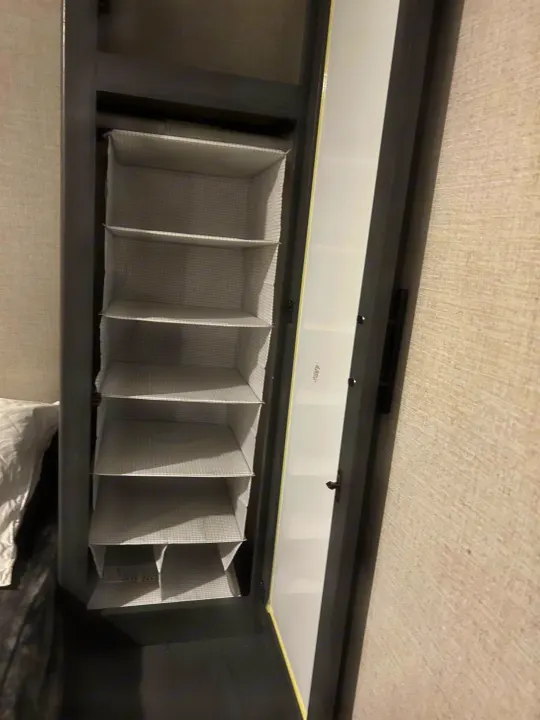 RV rental's narrow built-in closet with open door reveals tiered hanging fabric shelves for compact storage. Bedding visible left.. Dutchmen Aspen Trail LE 2022
