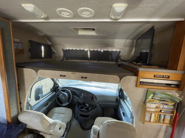 RV rental interior: front cockpit, overhead bunk, TV, and magazine rack with California travel guides. Ideal for road trips!. Jamboree Jamboree Motorhome 2006