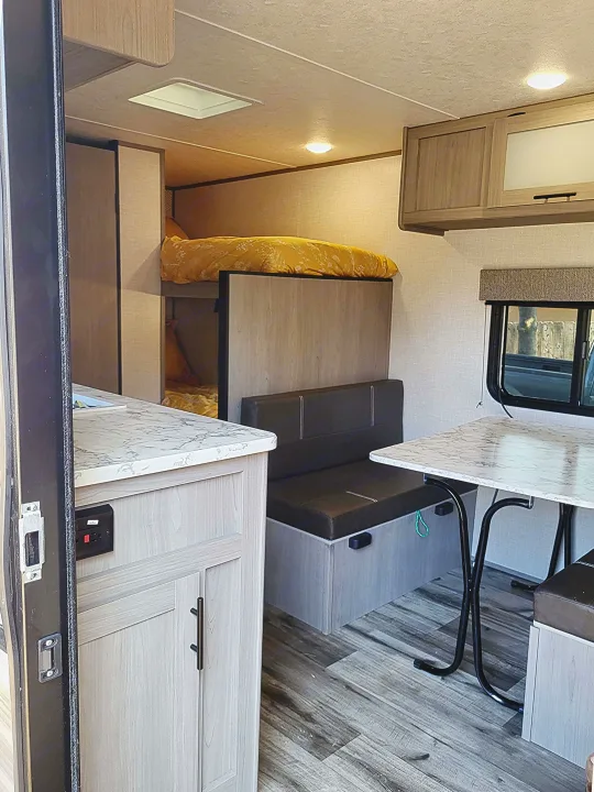 Spacious RV rental interior with modern design, featuring bunk beds, a dining area, and a functional kitchenette.. Dutchmen Coleman Lantern LT 2023