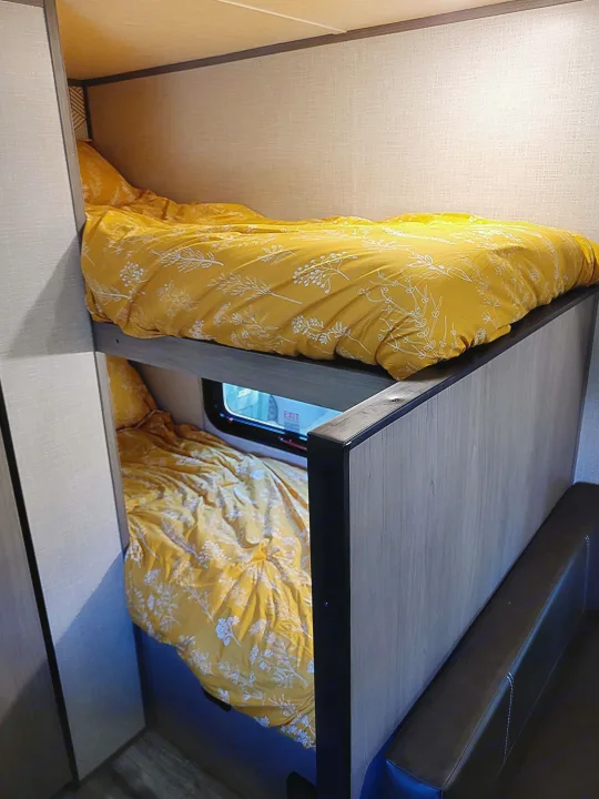 RV rental bunk beds feature cheerful yellow and white floral bedding, creating a cozy sleeping space inside.. Dutchmen Coleman Lantern LT 2023
