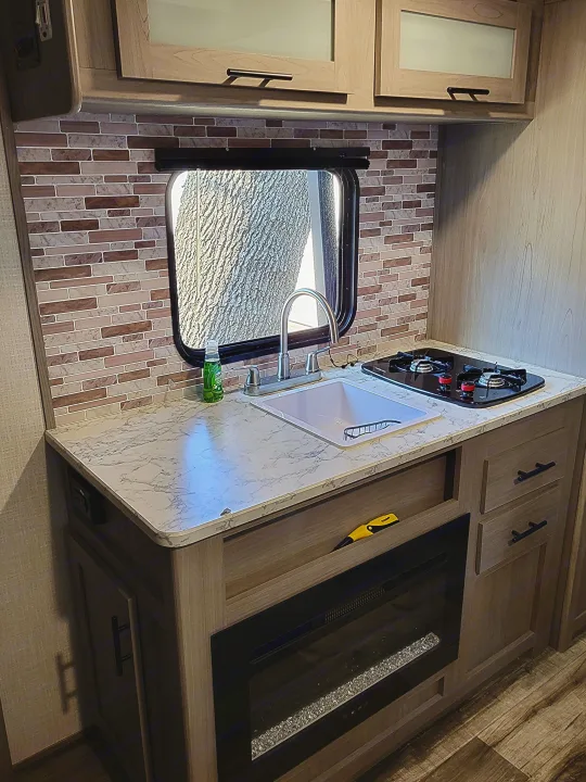 Step inside this RV rental's modern kitchen with a stylish backsplash, sink, stovetop, and cozy electric fireplace.. Dutchmen Coleman Lantern LT 2023