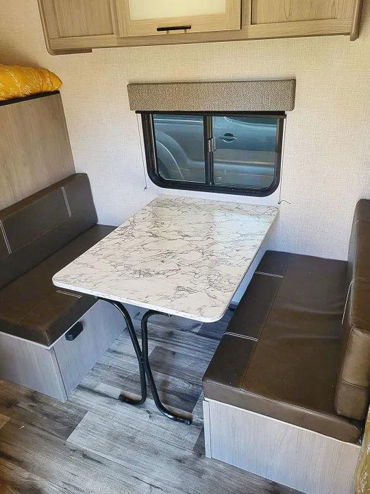 RV rental: Modern interior featuring a dinette with dark booth seating, a marble-patterned table, and overhead storage.. Dutchmen Coleman Lantern LT 2023
