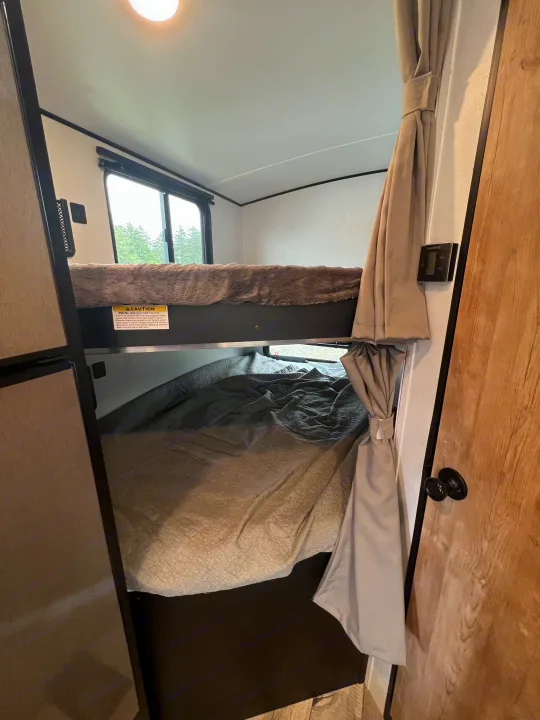 Inside an RV rental: two comfy bunk beds with a window view and a Dometic control. Top bunk is 300 lbs max.. Keystone RV Springdale 2022