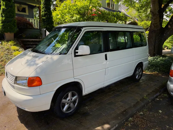 This white Volkswagen Eurovan camper, ideal for rv rental, is parked outside a house on a sunny day.. Volkswagen Westfalia 2003