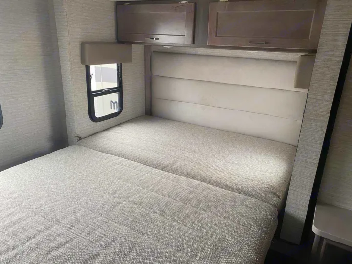 Modern RV rental sleeping area featuring a bed, padded headboard, overhead cabinets, and a window.. Winnebago Spirit 22M ( R25085) 2025