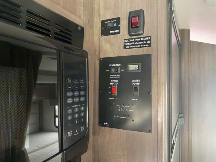 RV rental kitchen area showing a microwave and a control panel for generator, water, and tank levels. Essential RV systems.. Winnebago Spirit 22M ( R25085) 2025