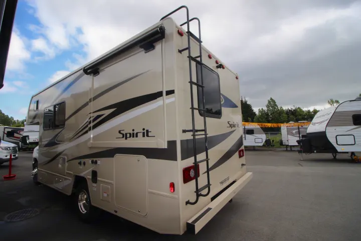 A tan Spirit RV for rent is parked in an outdoor lot, showing its side graphics, rear ladder, and other campers nearby.. Winnebago Spirit 22M ( R25085) 2025