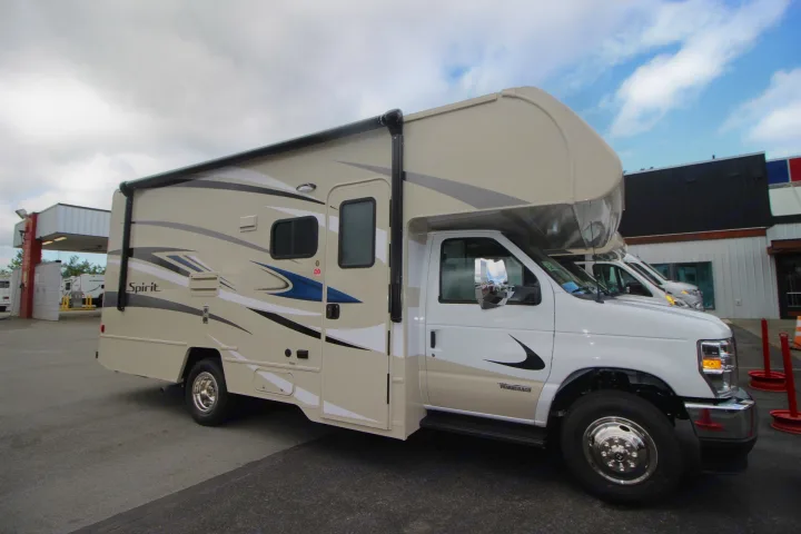 A beige and white Winnebago Spirit Class C RV, ideal for an rv rental, parked outside. Shows side awning and distinct graphics.. Winnebago Spirit 22M ( R25085) 2025