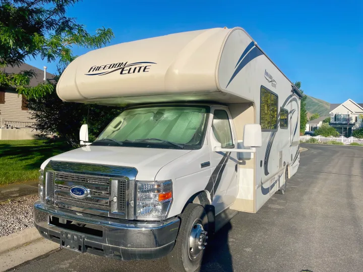 This white Freedom Elite Class C RV rental is parked on a sunny residential street, ready for a travel adventure.. Thor Freedom Elite 2019